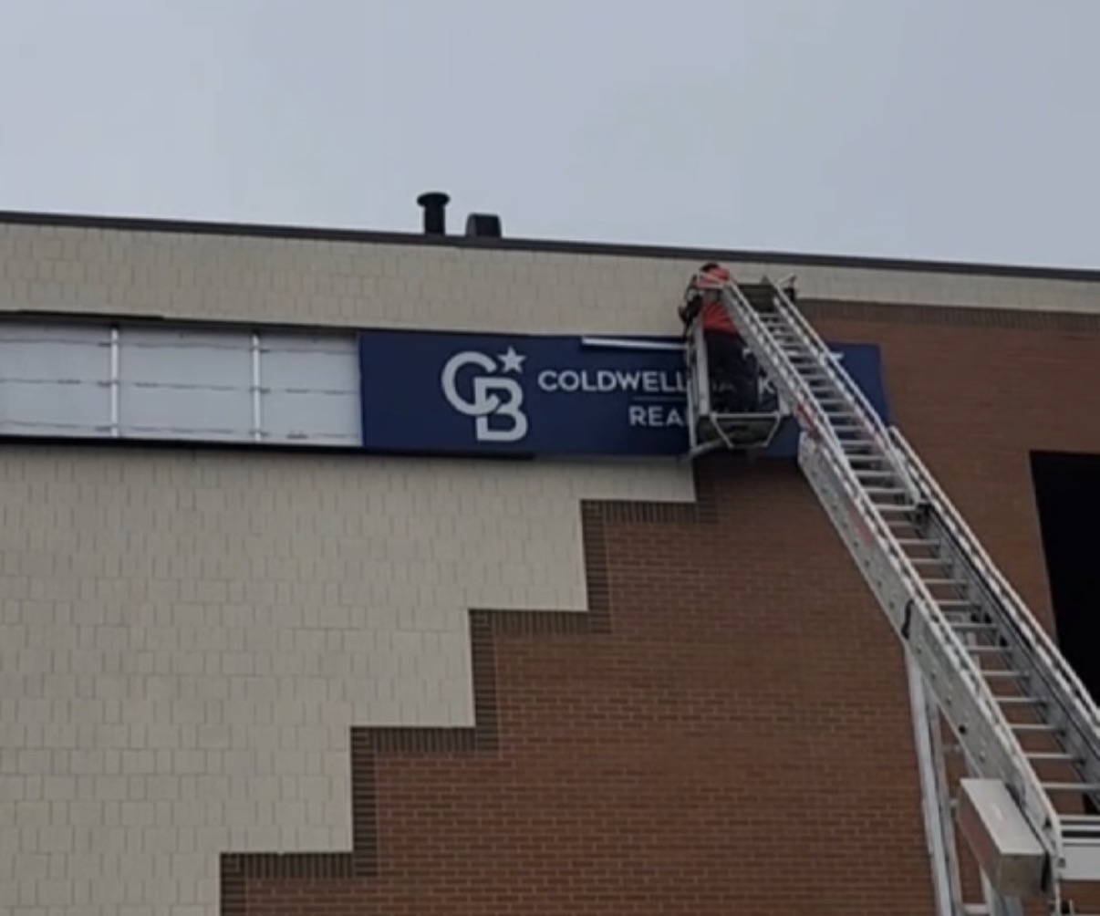 Installer on a ladder mounting a Coldwell Banker exterior building sign